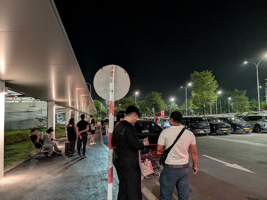 ノイバイ空港P1駐車場のGrab乗り場。屋根つきの歩道でベンチに座って待つ人と、車道に停まった配車待ちの車