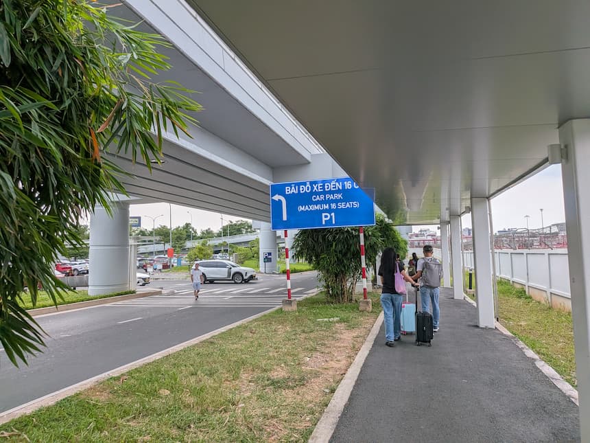ノイバイ空港T2の外にある「CAR PARK P1」の道路標識と、その方向へスーツケースを引いて歩く人たち