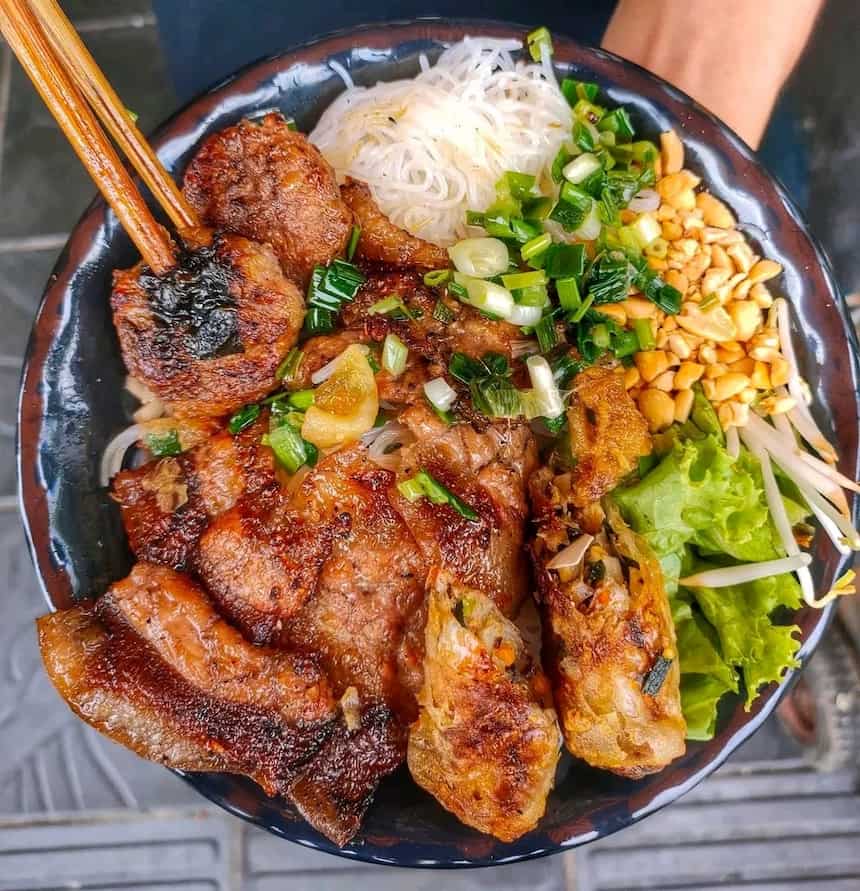 ハノイの「ブン・ティット・ヌオン(Bún thịt nướng)」。香ばしく焼かれた豚肉と揚げ春巻きがのった、新鮮な野菜とピーナッツのトッピングが相性抜群の冷たい麺料理です。