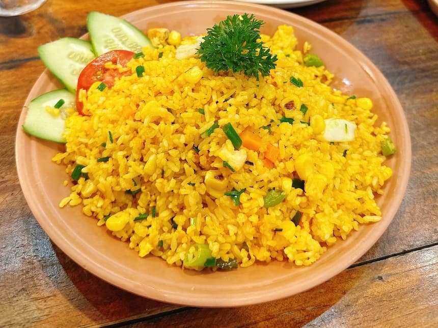 ベトナム風のチャーハン「コムチェン(Cơm chiên)」。黄金色に炒められたご飯に、人参、コーン、ネギなどの彩り豊かな具材が混ざり、キュウリとトマトを添えた食欲をそそる一品。
