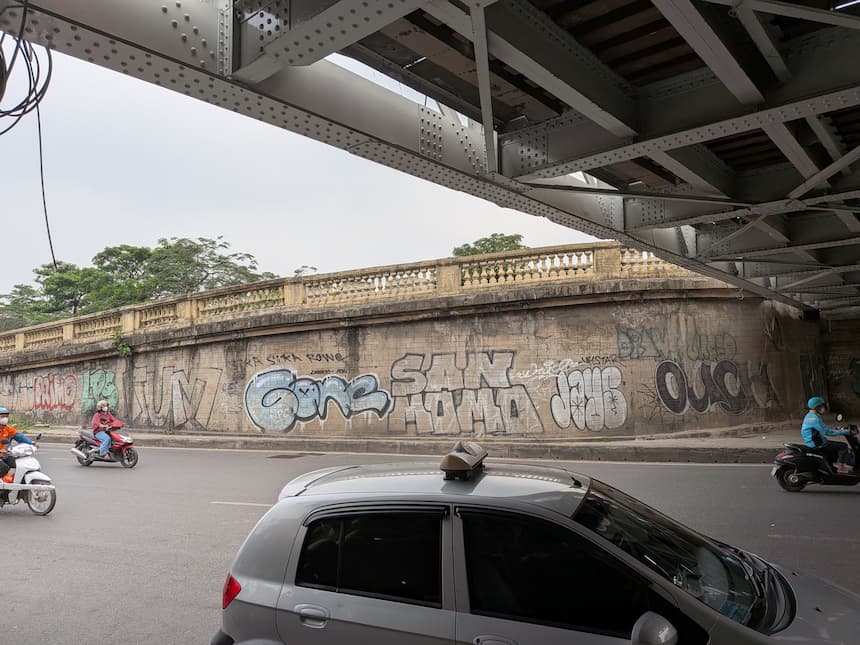 ハノイのロンビエン橋下の壁に描かれたグラフィティとバイクが行き交う風景