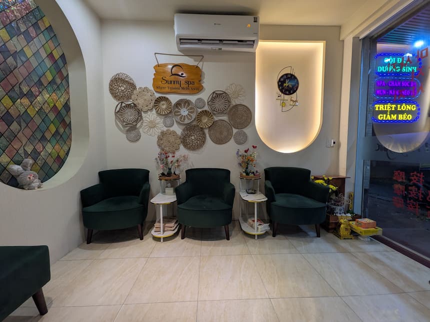 Sunny Spaの待合スペース。深緑のベルベットチェアとラタン製の壁飾りが並ぶ落ち着いた空間