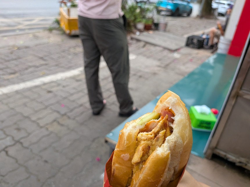 焼き卵をはさんだバインミー（バインミー・チュン）を手に持つ様子。屋台前の歩道にて