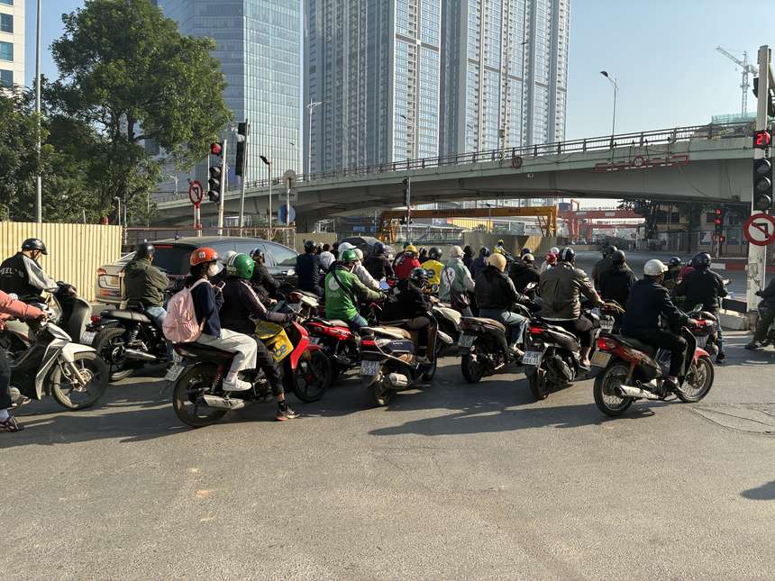ベトナムの都市の交差点で、赤信号待ちのバイクが密集している。背後には高架橋と高層ビル。
