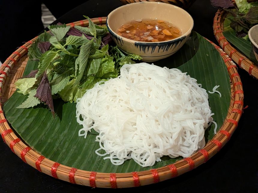 竹かごに盛られたブンチャー。バナナの葉の上に白いブン(米麺)と生ハーブ、甘酸っぱいヌクマムベースのつけダレの椀が並ぶハノイの名物料理。