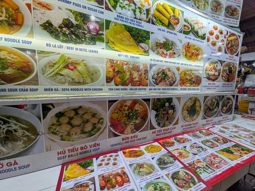 ベトナムの食堂の壁一面に貼られた写真付きメニュー。料理名と写真が並び、指差しで注文しやすい。BÚN RIÊUなどブン料理も並ぶ。