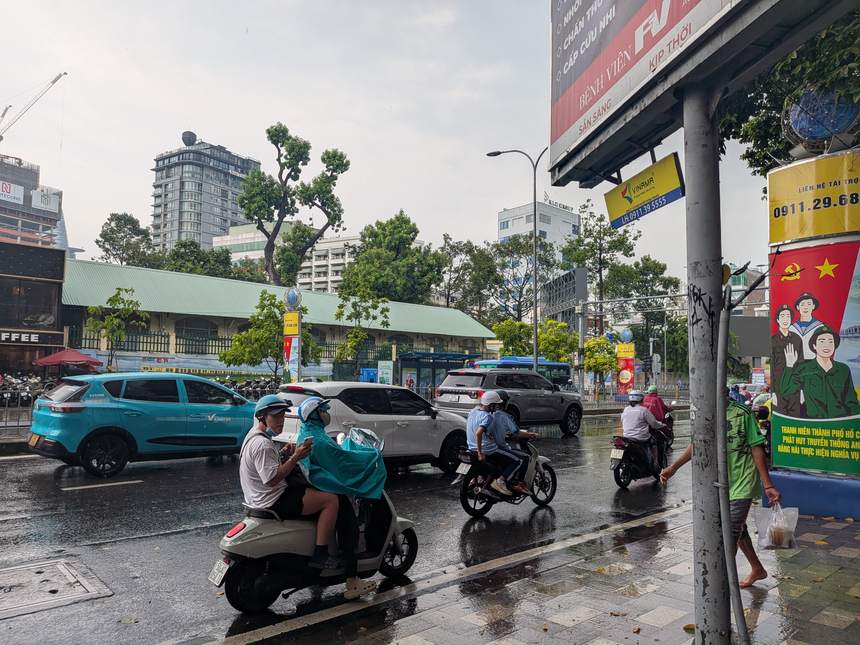 雨の降るベトナムの幹線道路で、緑のポンチョなど雨具を着たバイク乗りたちが濡れた路面を行き交う様子。午後のスコールはベトナムの雨季の日常。