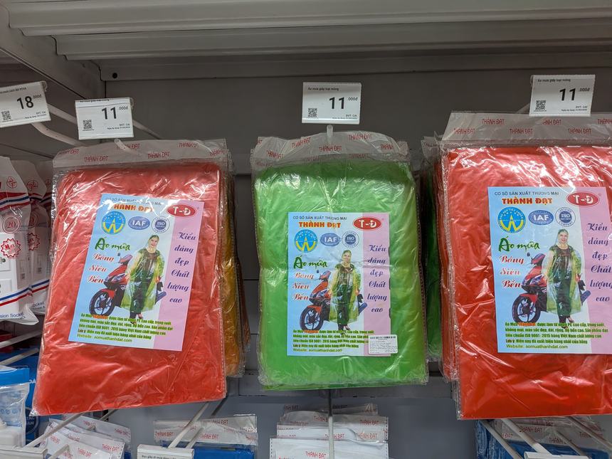ベトナムのスーパーの棚に並ぶバイク用レインコート。赤・緑・オレンジのパッケージで値札は1万1千ドン前後。雨季の旅行には必携の雨具。