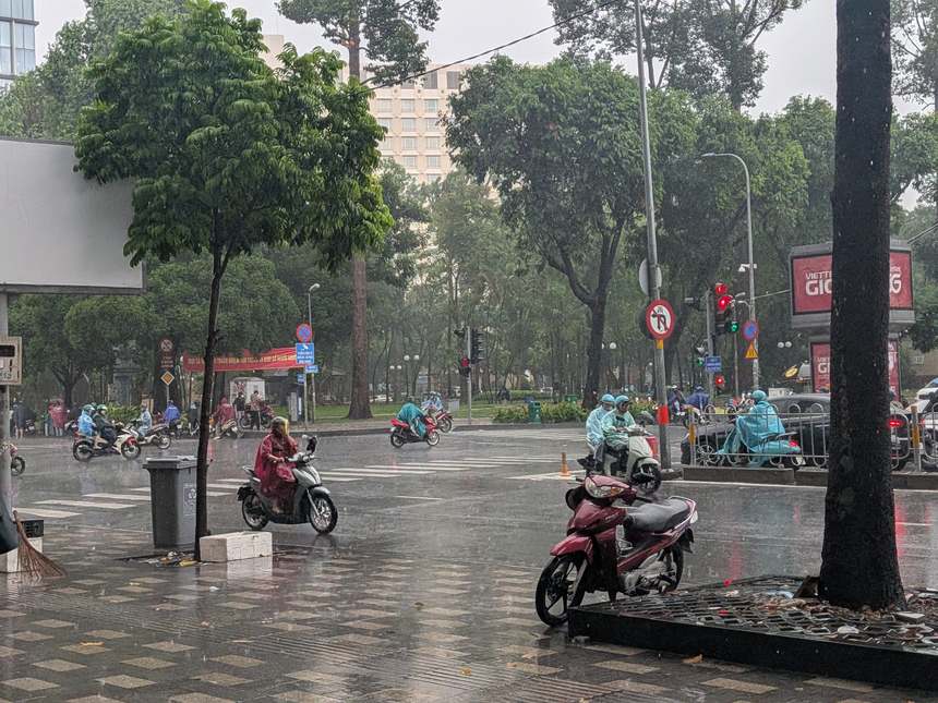 雨季のスコールの中、レインコート姿でバイクが行き交うベトナムの街の交差点