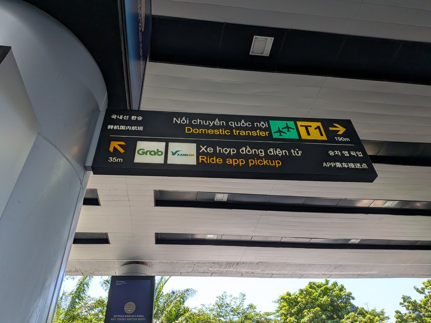 ベトナムの空港の屋外案内サイン。Grab等ライドアプリの乗車場所(35m先)や国内線乗り継ぎ(T1)が多言語で案内されている。