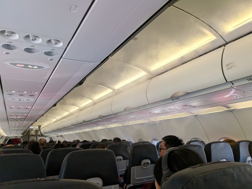 旅客機エコノミークラスの機内。頭上に手荷物の収納棚（オーバーヘッドビン）が並ぶ。