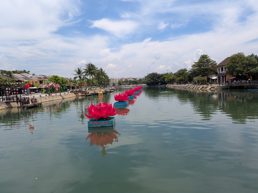 ホイアンのトゥボン川に浮かぶ蓮の花を模したフロート飾りと、対岸の黄色い街並み