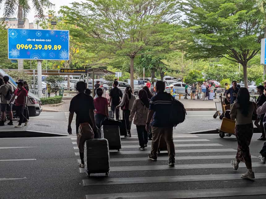 到着階から配車(ĐIỂM ĐÓN XE CÔNG NGHỆ/Ride Hailing)の乗り場へ横断歩道を渡る旅行者