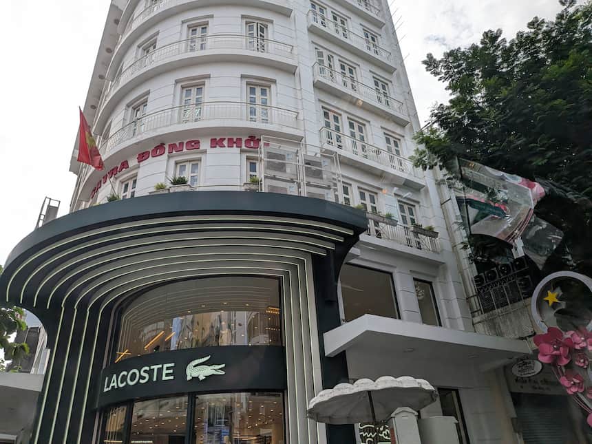 「ĐỒNG KHỞI(ドンコイ通り)」の街名標識とブランド店が並ぶ昼の通り