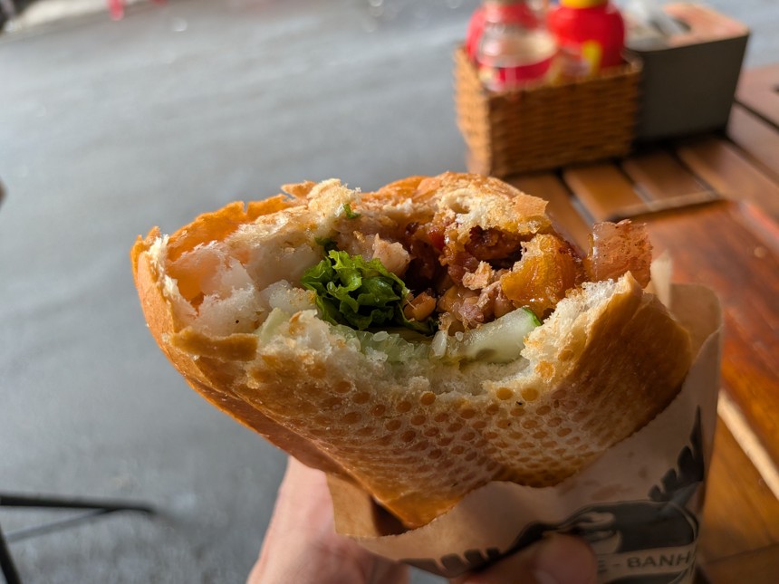 ペーパーに包まれたバインミーを手に持った様子。カリカリのフランスパンの中に野菜や肉などの具材がたっぷり詰まっており、ベトナムの定番ストリートフード。