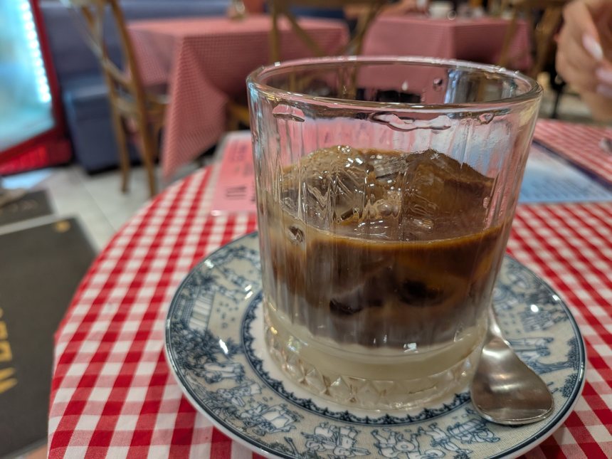 赤いギンガムチェックのテーブルクロスが敷かれたカフェで、ミルクとエスプレッソが層になったアイスコーヒーの飲み物がレトロなグラスに盛られて提供されている。