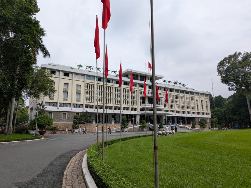 ホーチミン市の統一会堂(旧大統領官邸)の歴史的建造物。緑の芝生と赤い旗がたなびく広大な敷地が広がり、曇り空の下で荘厳な雰囲気を漂わせている。