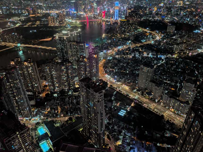 高層ビルの展望台から見下ろしたホーチミン市の夜景。サイゴン川沿いに広がる高層ビル群と幾筋もの光る道路が交差し、対岸には赤く輝く橋が映える壮大な都市夜景。