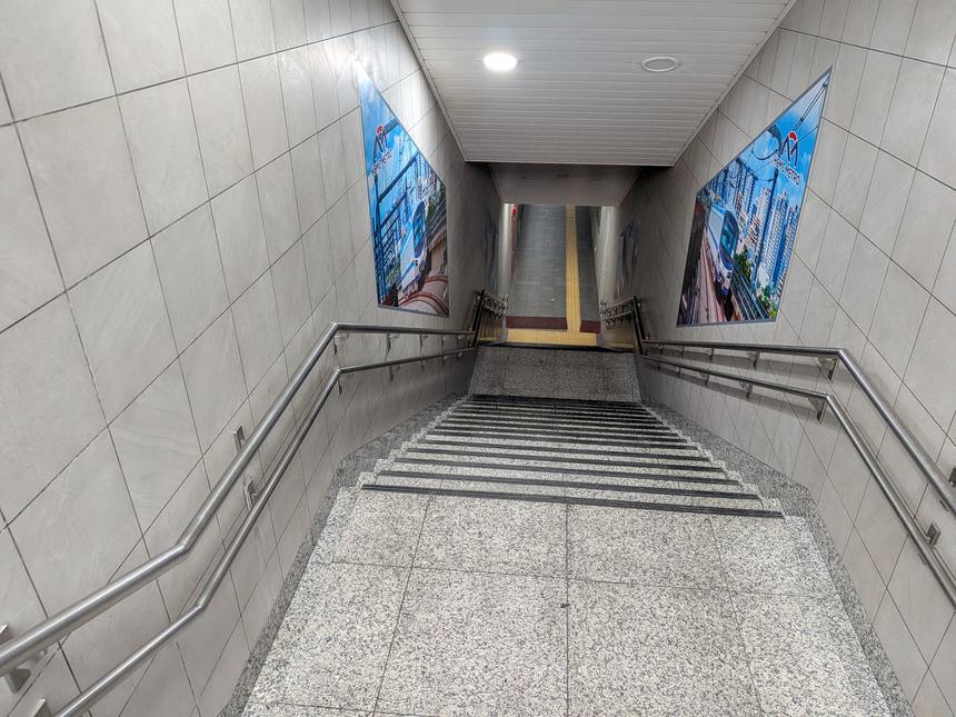 ホーチミン・メトロの駅出入口の階段。白いタイルの壁に都市景観の広告パネルが並ぶ近代的な地下通路