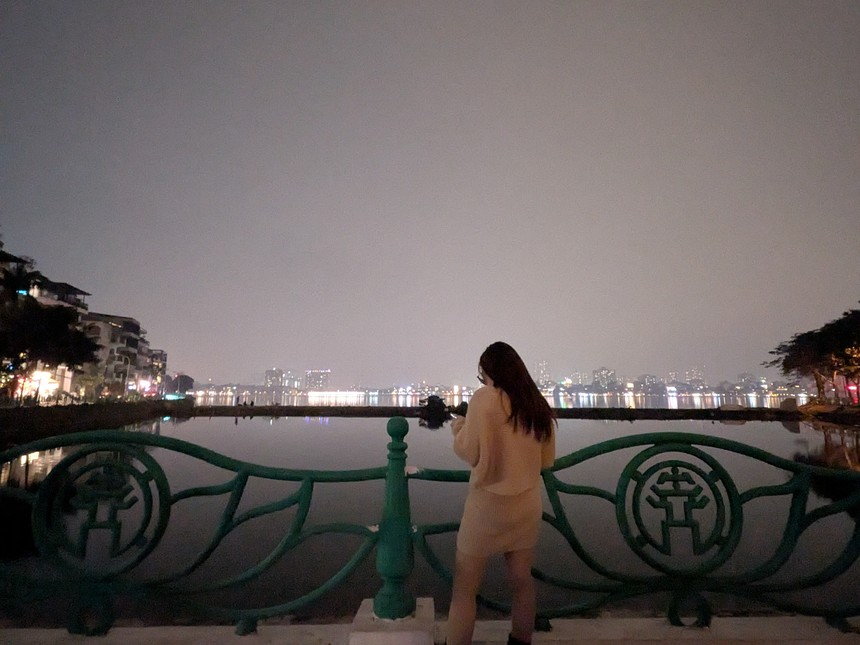 夜の湖畔で柵越しに街明かりを眺める女性の後ろ姿