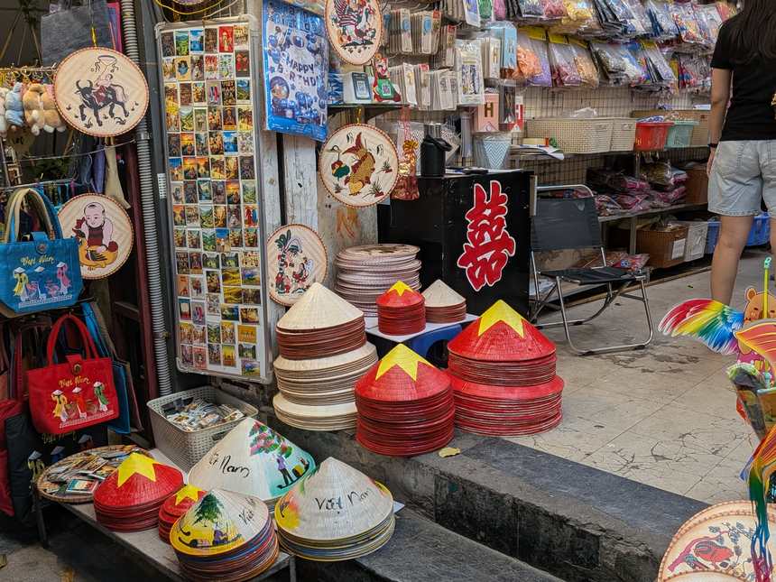 お土産店の店先に並ぶ色とりどりのノンラー（ベトナムの円錐笠）と刺繍プレート、ポストカード