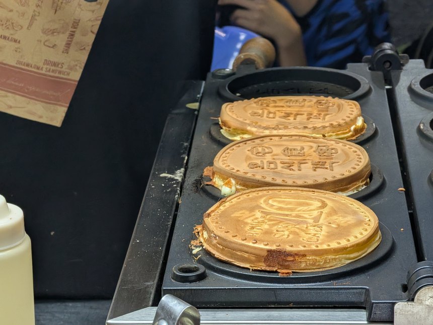 屋台の鉄板で文字の型押しが入った丸いワッフル状の焼き菓子(バイン)を焼く様子