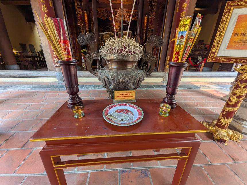 ベトナムの寺院の祭壇。赤漆塗りの台に銅製の香炉と立てられた線香、供え物の皿が並ぶ。