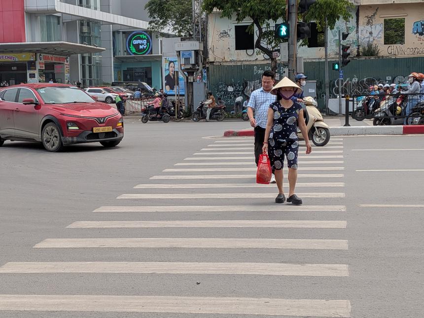 ベトナムの都市の交差点で、横断歩道を渡る歩行者。周囲をバイクや車が行き交う日常の光景。