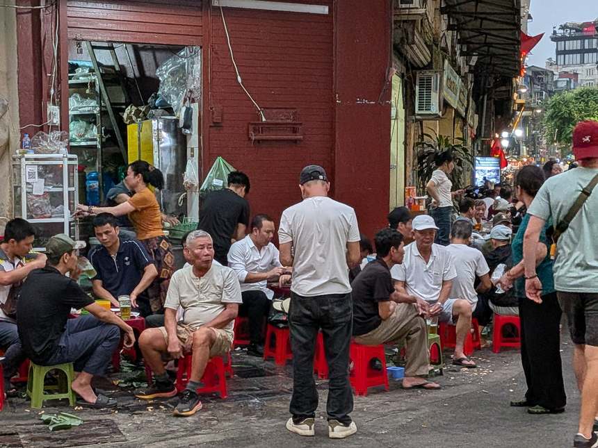 ベトナムの路上のビアホイ(生ビール店)。低いプラスチック椅子に腰掛けた人々が夕暮れの街角でくつろいでいる。