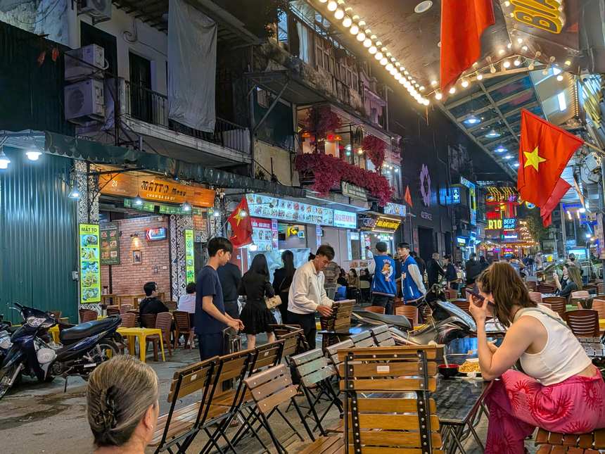ベトナムの夜のオープンエアの飲食街。ベトナム国旗が飾られた通りに木製のテーブルと椅子が並び、多くの人で賑わっている。