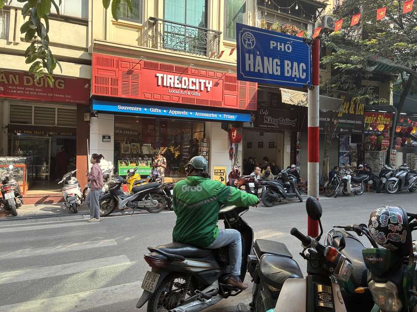 ハノイ旧市街のハンバック通りで、緑のユニフォームを着たGrabのバイクドライバーが客を待つ。配車アプリGrabはベトナム旅行の移動の定番。