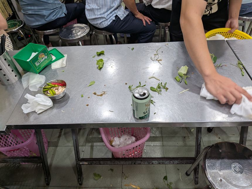 食べ終わった皿や野菜が残るステンレスの長机を、店員が布巾で拭いている様子