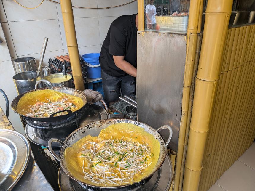 大きな中華鍋で焼かれているバインセオ。ターメリックで色づいた黄色い生地にもやしと青ねぎが乗っている