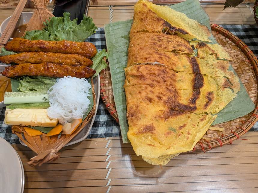 Mr. Bảy Miền Tâyのバインセオ一式。バナナの葉に乗った大判のバインセオと、ネムルイの串、ブン、きゅうり、にんじんの酢漬け