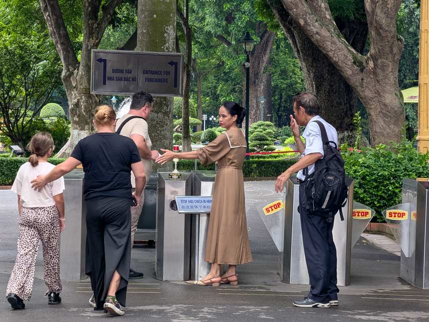 史跡エリアの外国人用入口。「ĐƯỜNG VÀO NHÀ SÀN BÁC HỒ／ENTRANCE FOR FOREIGNERS」の案内板の下にSTOP表示のゲートが並び、係員が見学者を通している