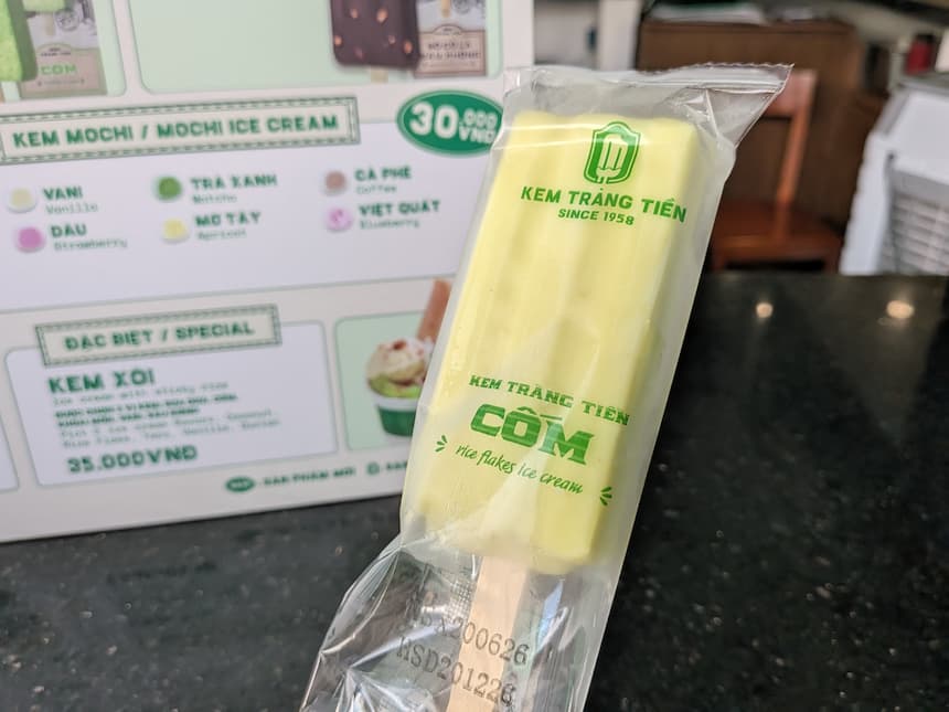 ケムチャンティエンのコム(緑もち米)の棒アイス。淡い黄緑色で、パッケージに『rice flakes ice cream』の文字