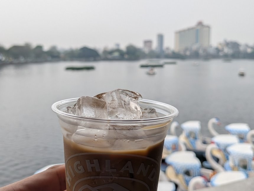 ハノイの湖のスワンボートを背景に持ったハイランズコーヒーのカップ