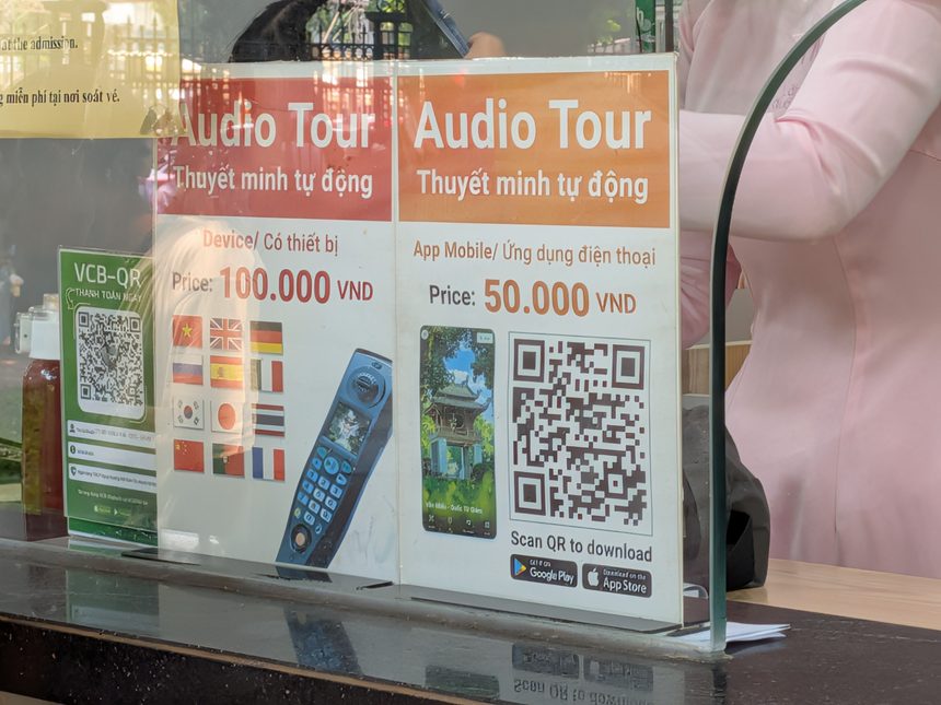 チケット売り場に置かれたオーディオガイドの料金案内。専用機器が100,000ドン、スマホアプリが50,000ドンで、対応言語の国旗に日本も並んでいる。