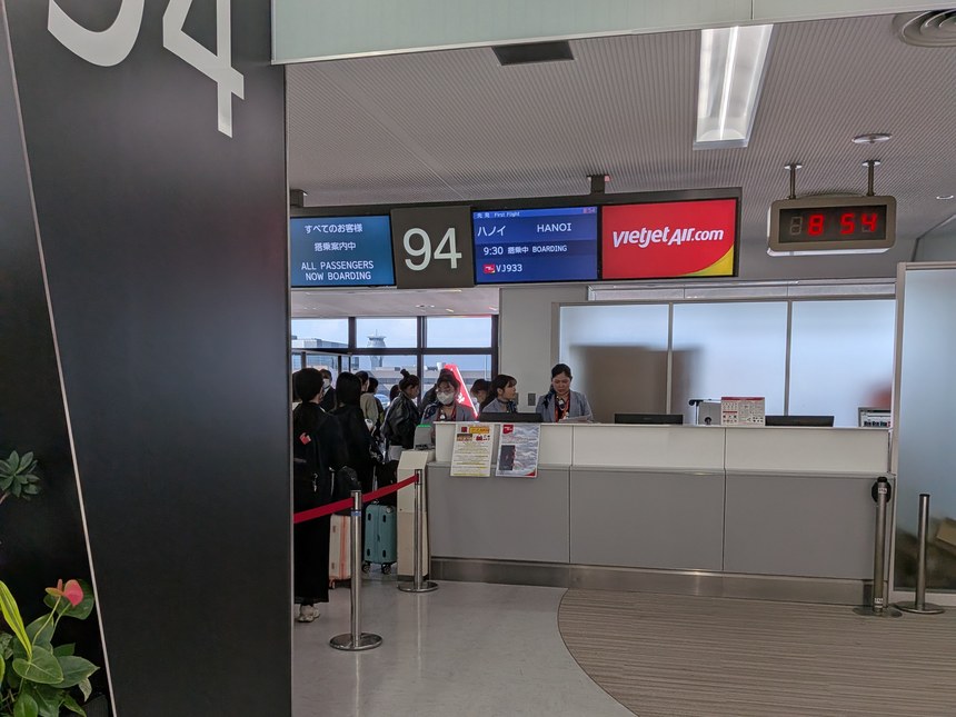 成田空港94番ゲートのベトジェット。ハノイ行きVJ933便が9時30分発で「すべてのお客様 搭乗案内中」と表示され、ゲート脇の時計は8時54分を指している。