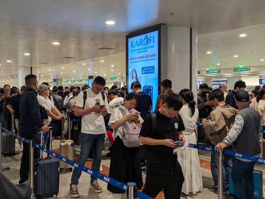 ベトナムの空港で出国審査の順番を待つ乗客の列。仕切りテープに沿って長い列ができ、多くの人がスマートフォンを見ながら待っている。