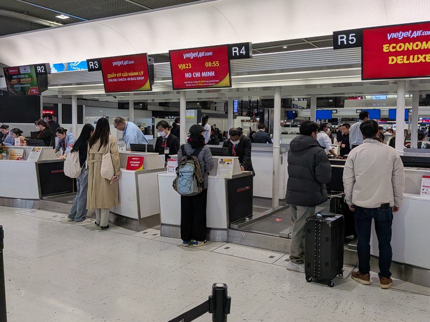 成田空港のベトジェットのチェックインカウンターR2〜R5。ホーチミン行きVJ823便の案内が出ており、オンラインチェックイン済みの乗客も手荷物預けの列に並んでいる。
