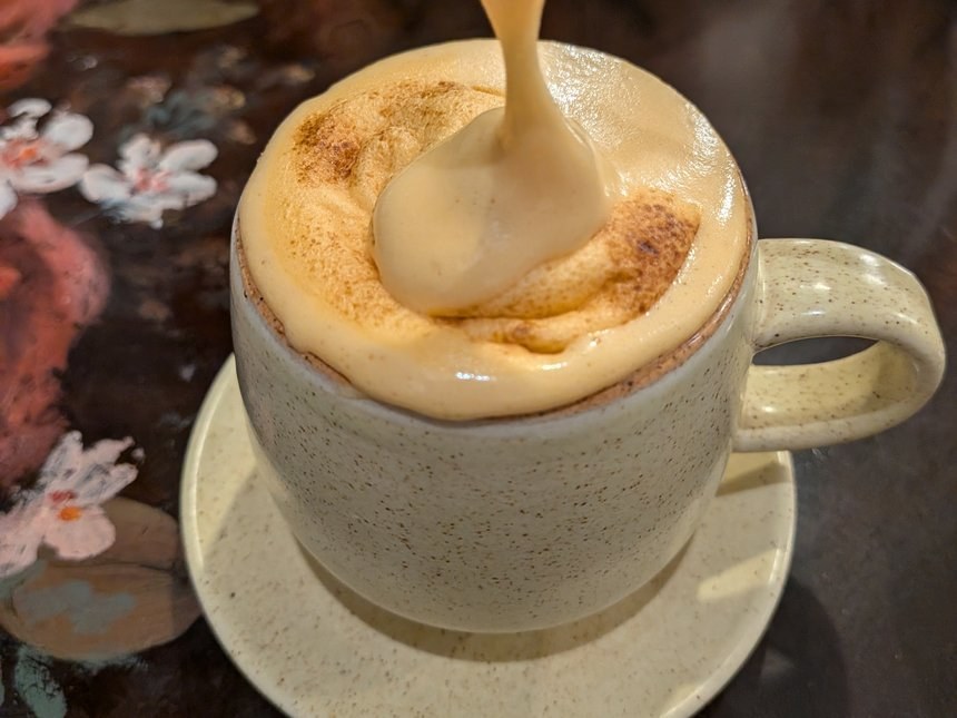 ベトナムのエッグコーヒー。スプーンですくった卵黄のクリームが、シナモンをかけた表面に糸を引いて落ちるところ。