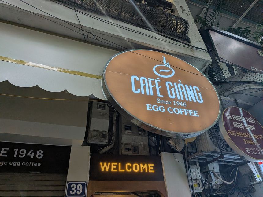 Cafe Giảngの入口。丸い看板に「CAFÉ GIẢNG Since 1946 EGG COFFEE」とあり、下に番地39の青いプレートが見える。