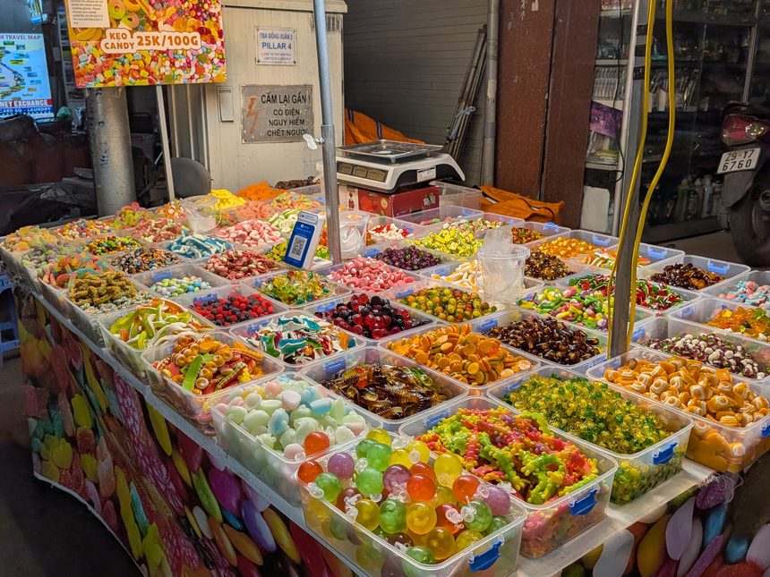 ベトナムの市場の量り売りキャンディー売り場と100グラムあたりの単価の看板