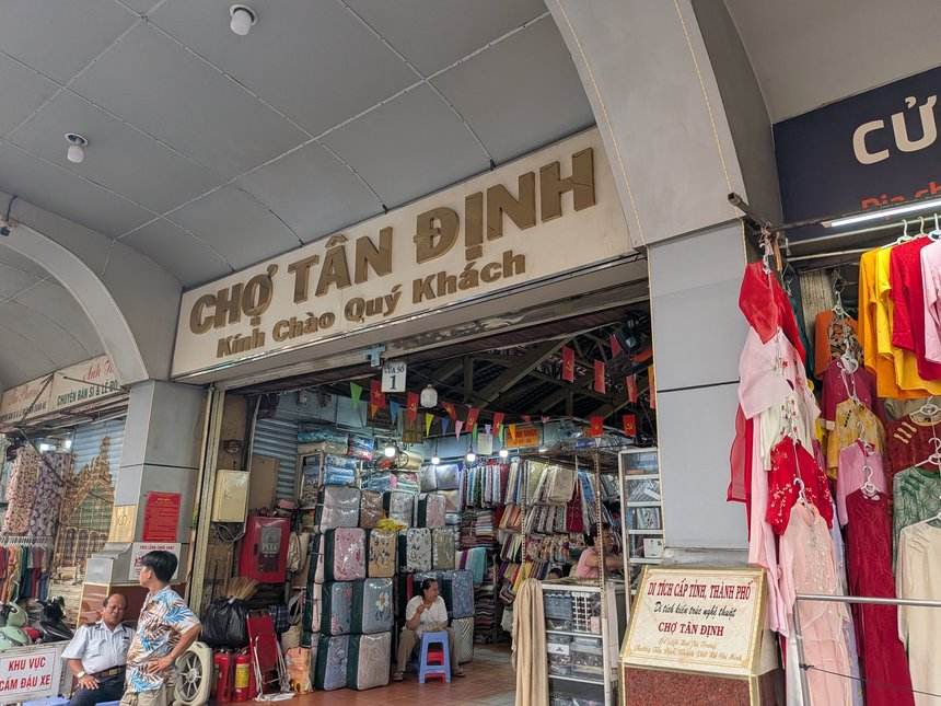 タンディン市場の入口。CHỢ TÂN ĐỊNH と書かれた看板の下に、布地の店が並んでいる
