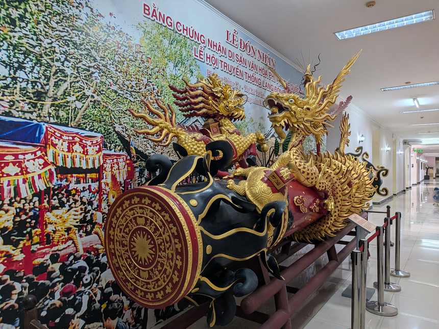 ベトナム国立歴史博物館の2号館の廊下。金色の龍が巻きついた黒い筒の模型が置かれ、後ろの壁に祭りの写真が貼られている