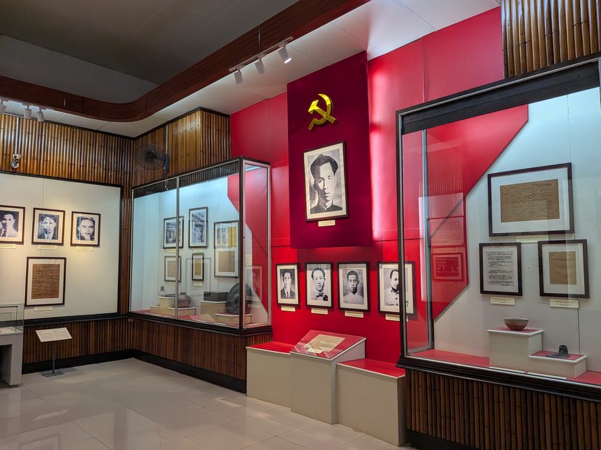 ベトナム国立歴史博物館の2号館の展示室。赤い壁に鎌と槌の印と肖像が掛かり、ガラスケースに写真や文書が並ぶ