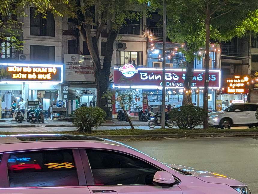 夜の通り。左に「BÚN BÒ NAM BỘ」「BÚN BÒ HUẾ」の光る看板の店、中ほどに「Bún Bò」の文字の赤い看板の店が並ぶ