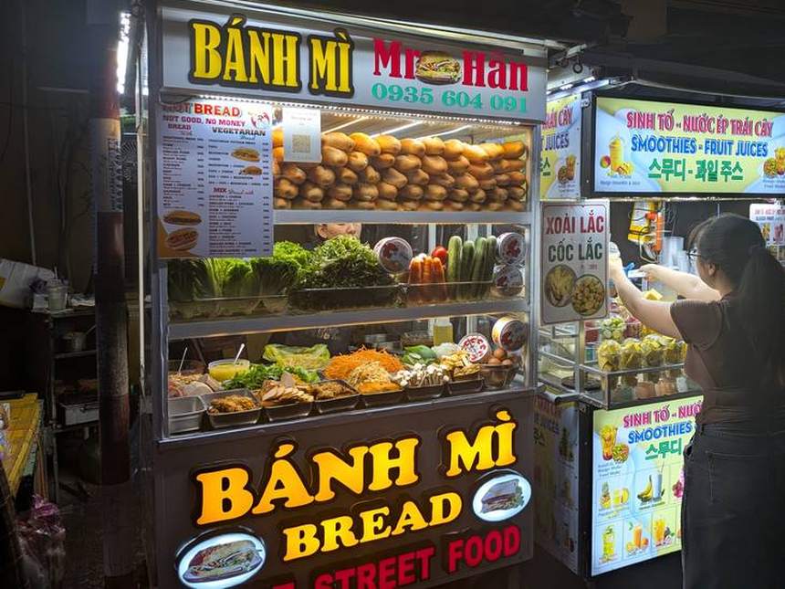 夜の屋台街に並ぶバインミーの屋台「BÁNH MÌ Mr Hân」。ガラスケースにパンと野菜、具が並んでいる