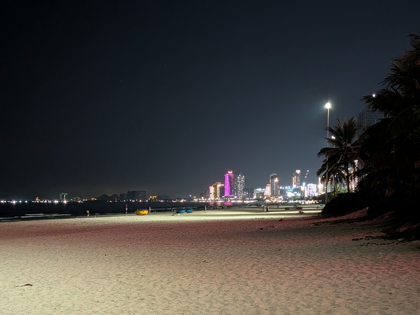 夜の浜。街灯に照らされた砂浜と、海沿いに並ぶ光る高層ビル